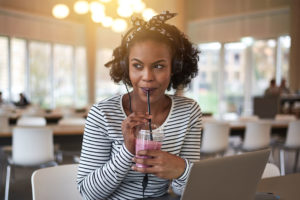 Young diverse woman with headphones, sitting in a cafe sipping a smoothie.