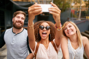 Three diverse friends smiling taking a selfie in front of a store. 