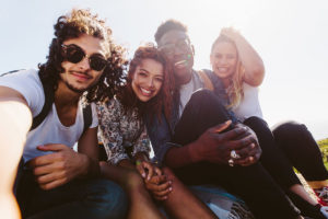 A group of 4 diverse students smiling taking a selfie on a sunny day. 